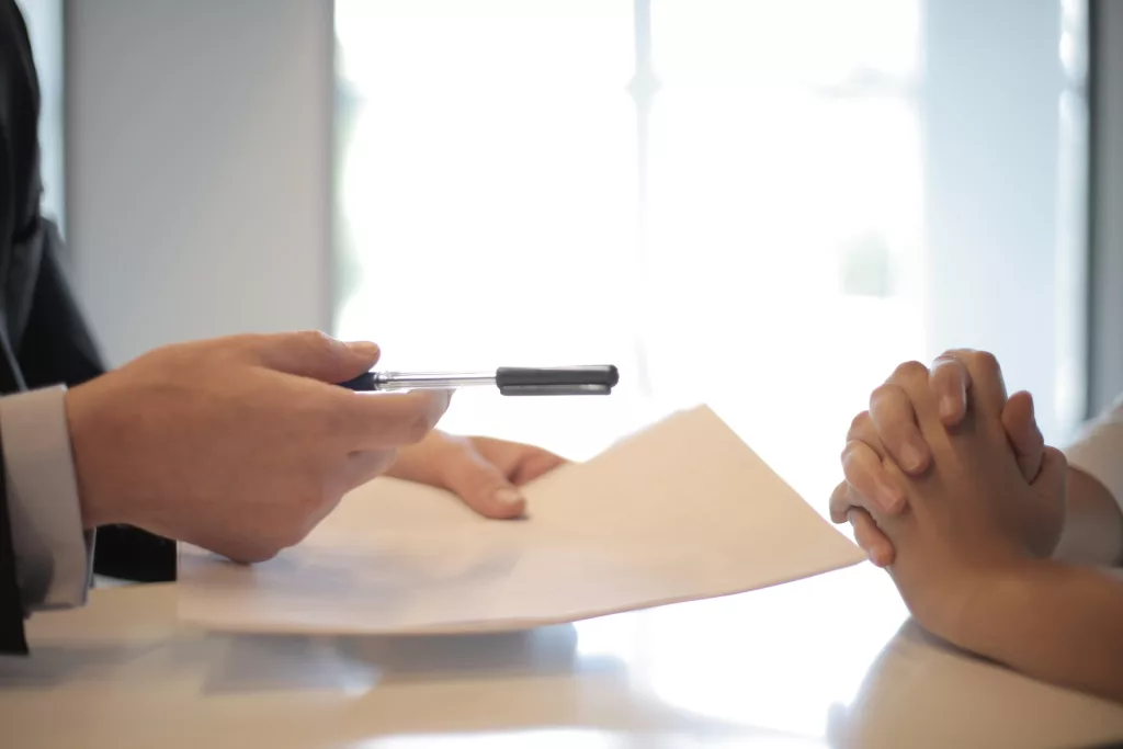 One person holds out a pen and paper to the other to sign 