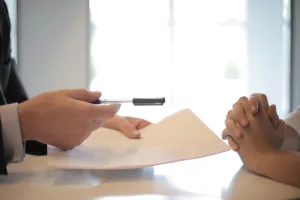 One person holds out a pen and paper to the other to sign